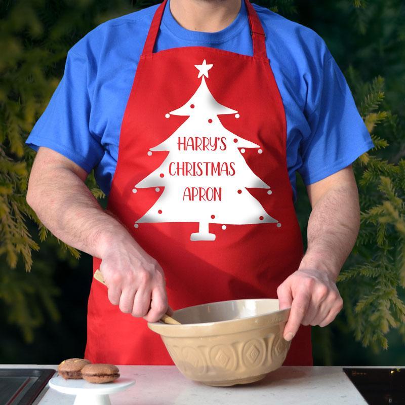 A personalised red Christmas apron. the apron has a Christmas tree design printed on it and the words "Harry's Christmas apron"