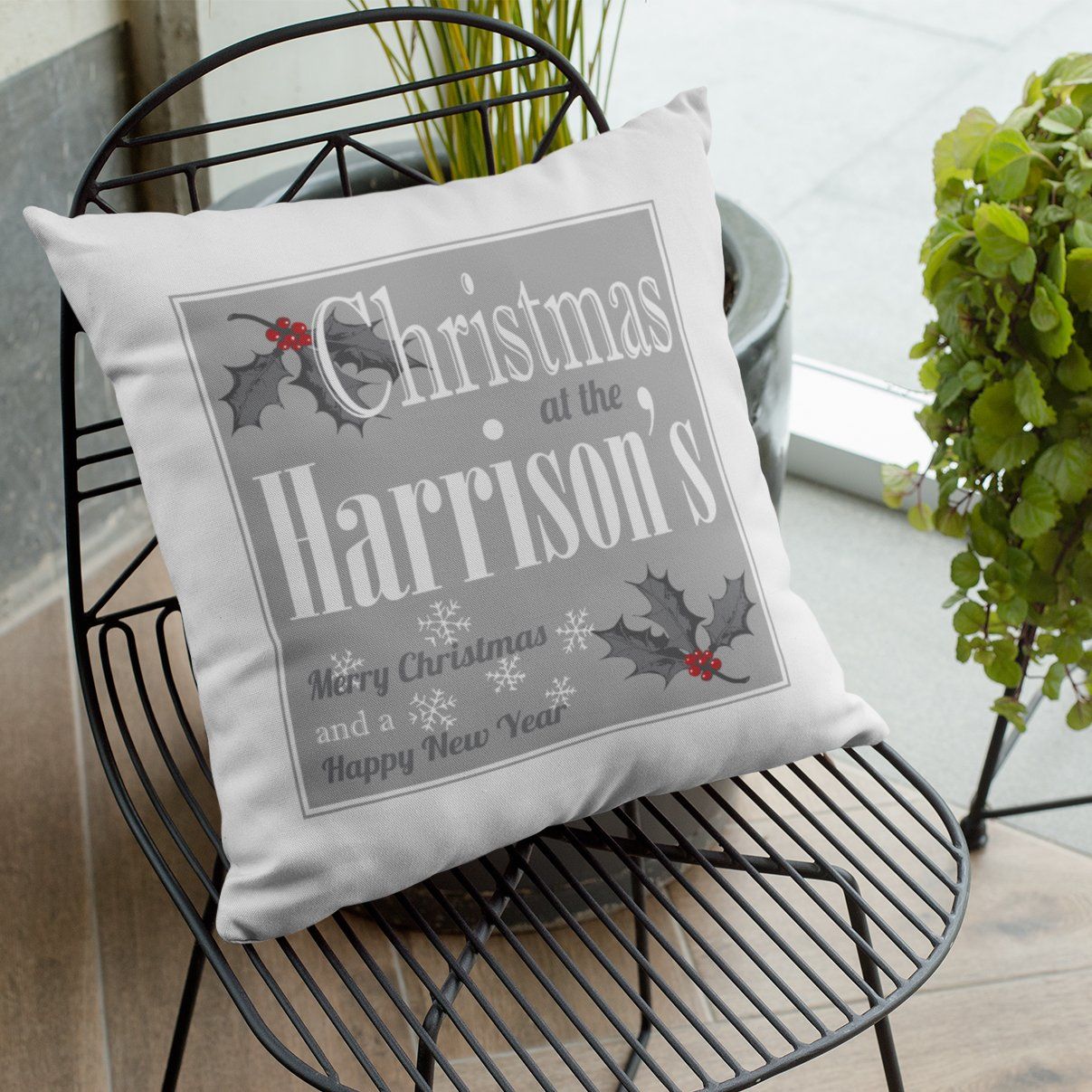 A personalised white, grey and red Christmas cushion with a text based design and holly leaf illustrations