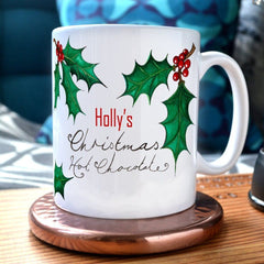 A personalised Christmas mug with the message "Holly's Christmas Hot Chocolate" and illustrations of holly leaves printed onto it.