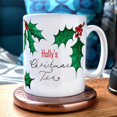 A personalised Christmas mug with the message "Holly's Christmas Tea" and illustrations of holly leaves printed onto it.