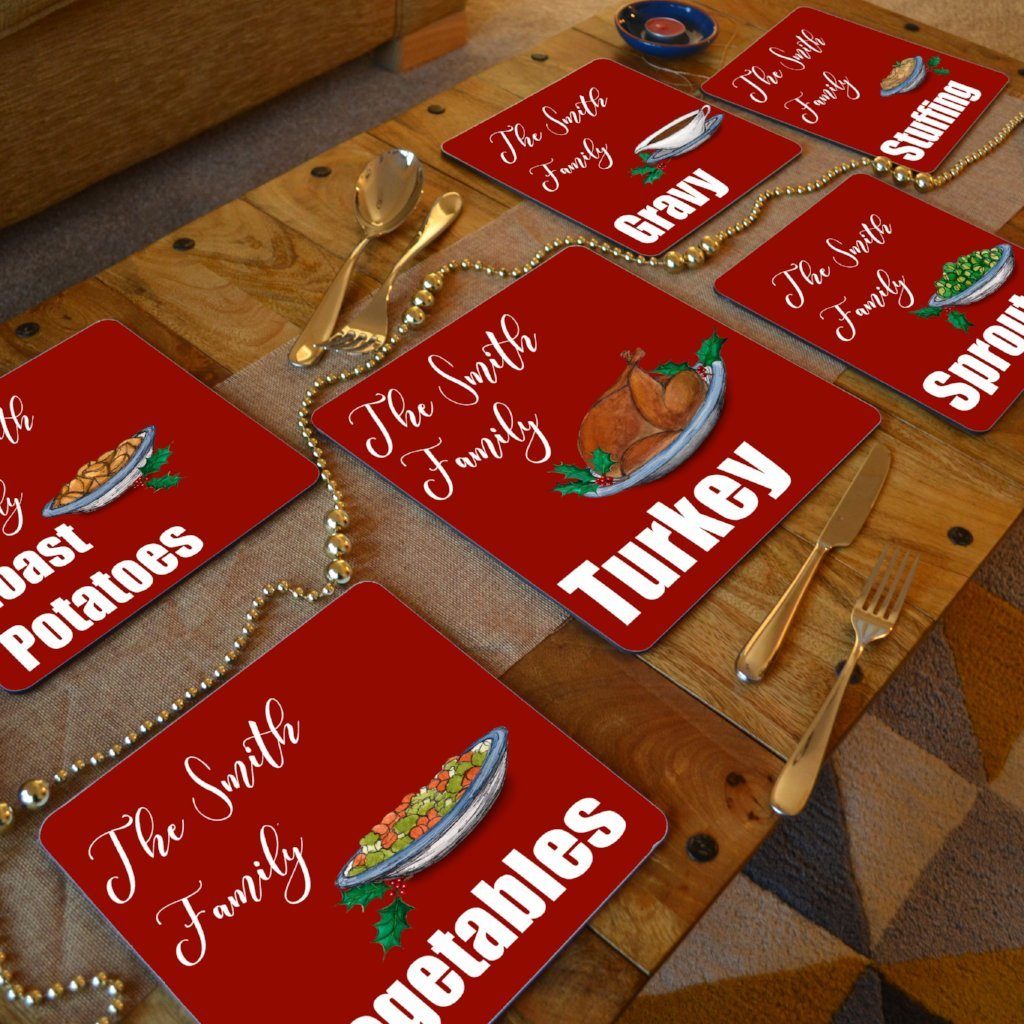 A dining table with personalised Christmas placemats on. The placemats are red with white text and illustrations of Christmas food