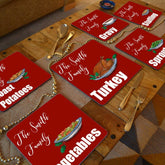 A dining table with personalised Christmas placemats on. The placemats are red with white text and illustrations of Christmas food