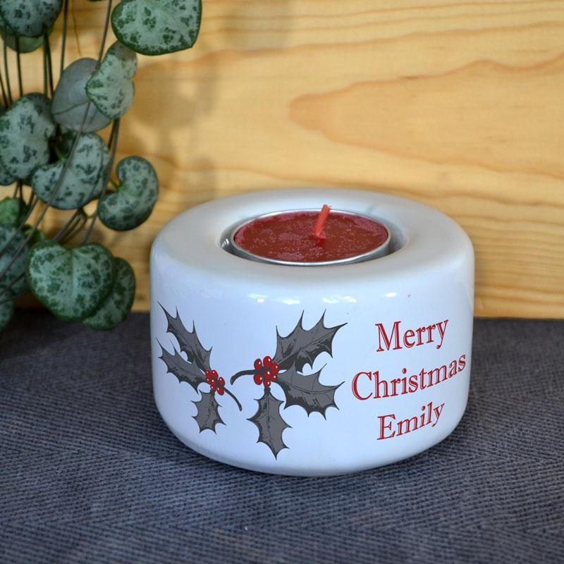 A personalised christmas candle holder in white with a holly leaf design and custom lettering in red.