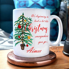 A personalised mug with the words "It's beginning to look a lot like Christmas" printed on in a red italic font. The mug also has an illustration of a Christmas tree and the name "Aimee" printed on it