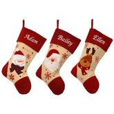 3 personalised Christmas stockings in a row. The stockings are made from natural calico and have red felt tops heals and toes. Each one has a character on, one with a Santa, one with a snowman and one with a reindeer. The stockings have an embroidered name at the top in white lettering.