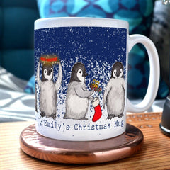 A personalised penguin Christmas mug. The design on the mug shows 4 baby penguins doing different Christmas activities. The mug is personalised with the words "Emily's Christmas Mug"