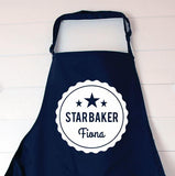 A navy blue personalised apron with a white circular design printed on the front. The design features 3 stars at the top, and the words "star baker Fiona" 