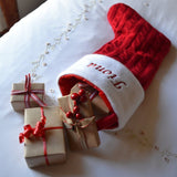 a personalised knitted Christmas stocking on the end of a bed with presents inside 