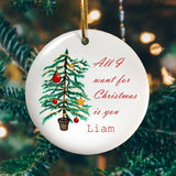 A personalised circular ceramic Christmas decoration with an illustration of a Christmas tree and the words "All I want for Christmas is you Liam" in red script text printed onto it.