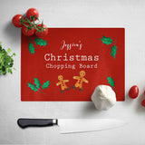 A personalised Christmas chopping board. The chopping board has a red background and a pattern of gingerbread men and holly leaves. The design includes white text which reads "Jessica's Christmas chopping board" 