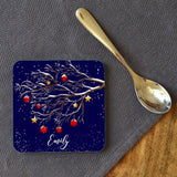 A personalised Christmas coaster on a table next to a tea spoon