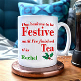 A personalised Christmas mug in white with a red message printed on it and an illustration of holly leaves