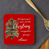 A personalised red square coaster with an illustration of a Christmas tree and the words "it's beginning to look a lot like Chrsitmas" printed onto it. The coaster is customised with the name "Aimee" 