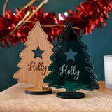 Two personalised Christmas decoration cut in a tree shape. One is made from oak and one is made from green acrylic.
