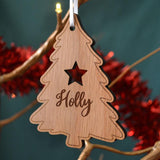 A personalised oak Christmas tree decoration which has been cut in a tree shape. The tree has a star and a name on the front.